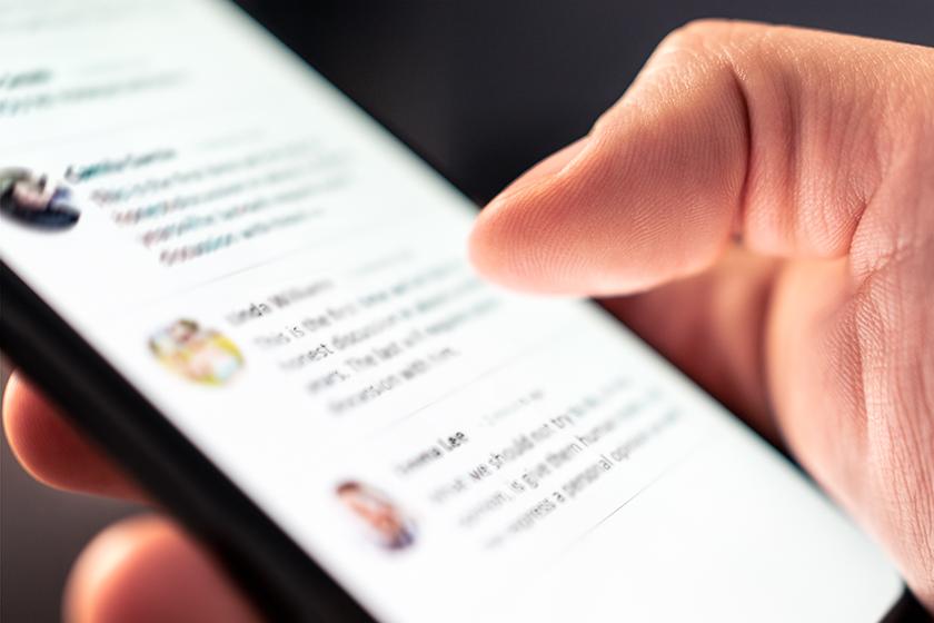 Man holding a phone in his hands with some social media app comments displaying on screen.