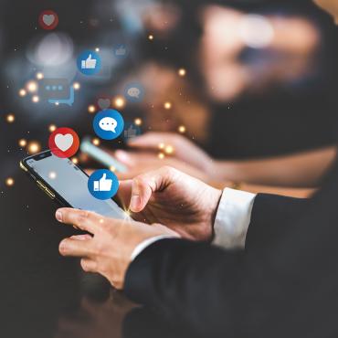 Business man holding a phone in his hands, with likes and thumbs-up social media icons flying around